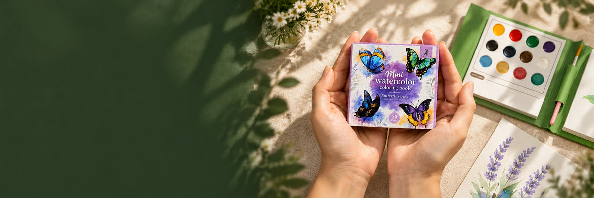 A butterfly mini watercolor book held in two hands on a warm art table